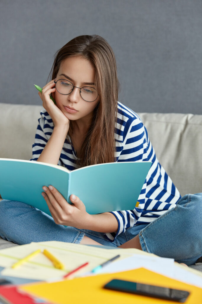 concentrated woman in optical glasses, thinks on creative ideas for publication, holds pen for writing, makes notes, has leisure time at home poses in living room at desktop with papers and literature concentrated woman in optical glasses, thinks on creative ideas for publication, holds pen for writing, makes notes, has leisure time at home poses in living room at desktop with papers and literature